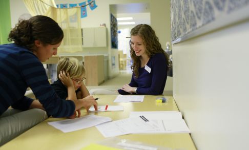 A speech therapy student works with a child and their adult in a speech pathology clinic.