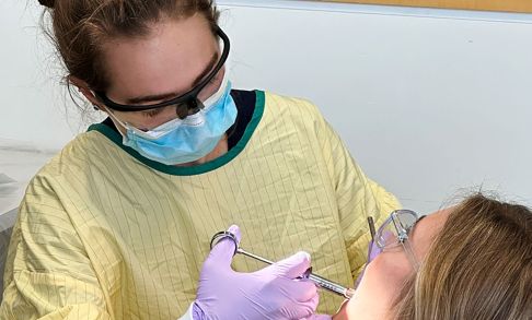Alex Hays in yellow gown practicing giving a shot to a patient.