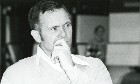 Photo of Mike Clock sitting and coaching, his left hand in front of his face.