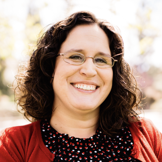 A white woman with brown hair and glasses smiling at the camera.