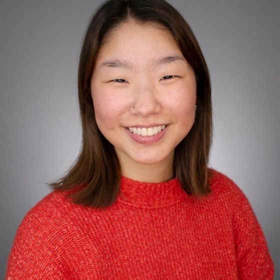 Yoorim wears a red sweater in front of a grey background.