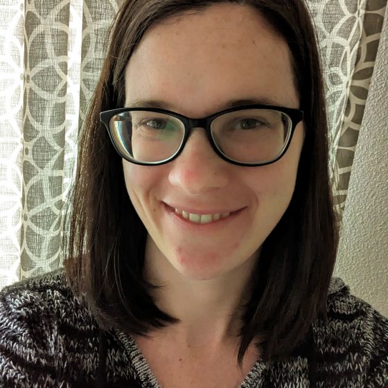 Headshot of woman with dark shoulder length hair with glasses.