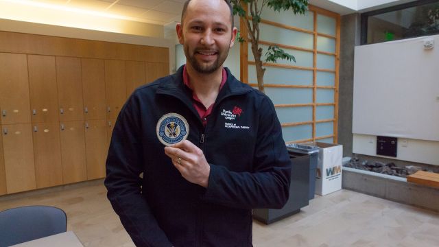 Mark Loomis OTD '17 holds up his rescue swimmer patch at the Hillsboro Campus