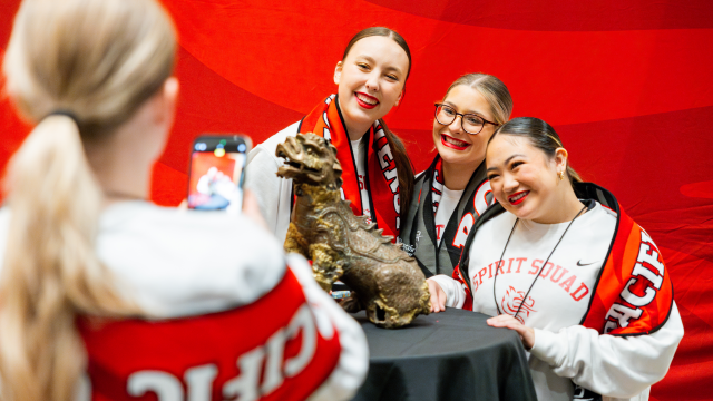 Three Pacific students wearing Boxer scarves pose with the Boxer statue while a fourth student takes their photo on a phone