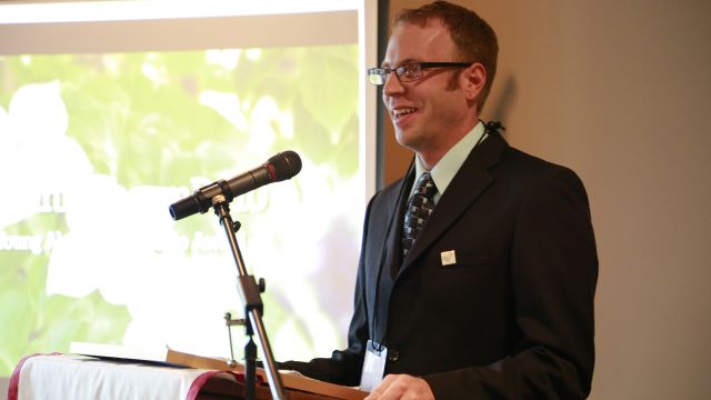 Alex Winn stands at a podium during the Alumni Awards ceremony