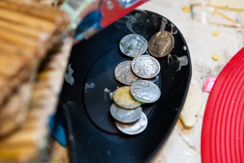 A black rubber spoon holds a small pile of buffalo nickels covered with droplets of dried wax.