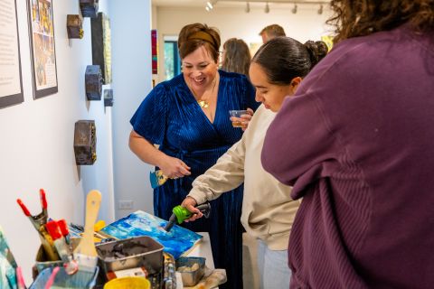 Stevie Woods watches as student holds a blowtorch next to an unfinished canvas.