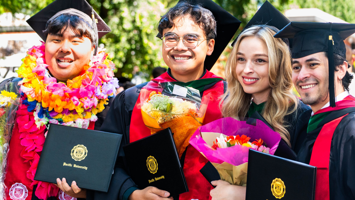Four Pacific University graduates pose in caps, gowns and leis with their diploma covers
