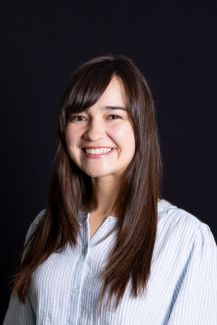 A photograph of Olivia smiling with brown hair wearing a blue and white-striped blouse. 