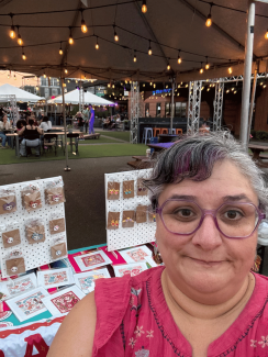 Headshot of a woman wearing glasses and a pink top smiling in an outdoor market setting.