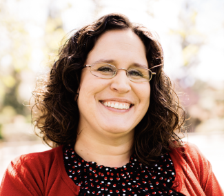A white woman with brown hair and glasses smiling at the camera.