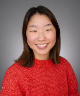 Yoorim wears a red sweater in front of a grey background.