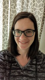 Headshot of woman with dark shoulder length hair with glasses.