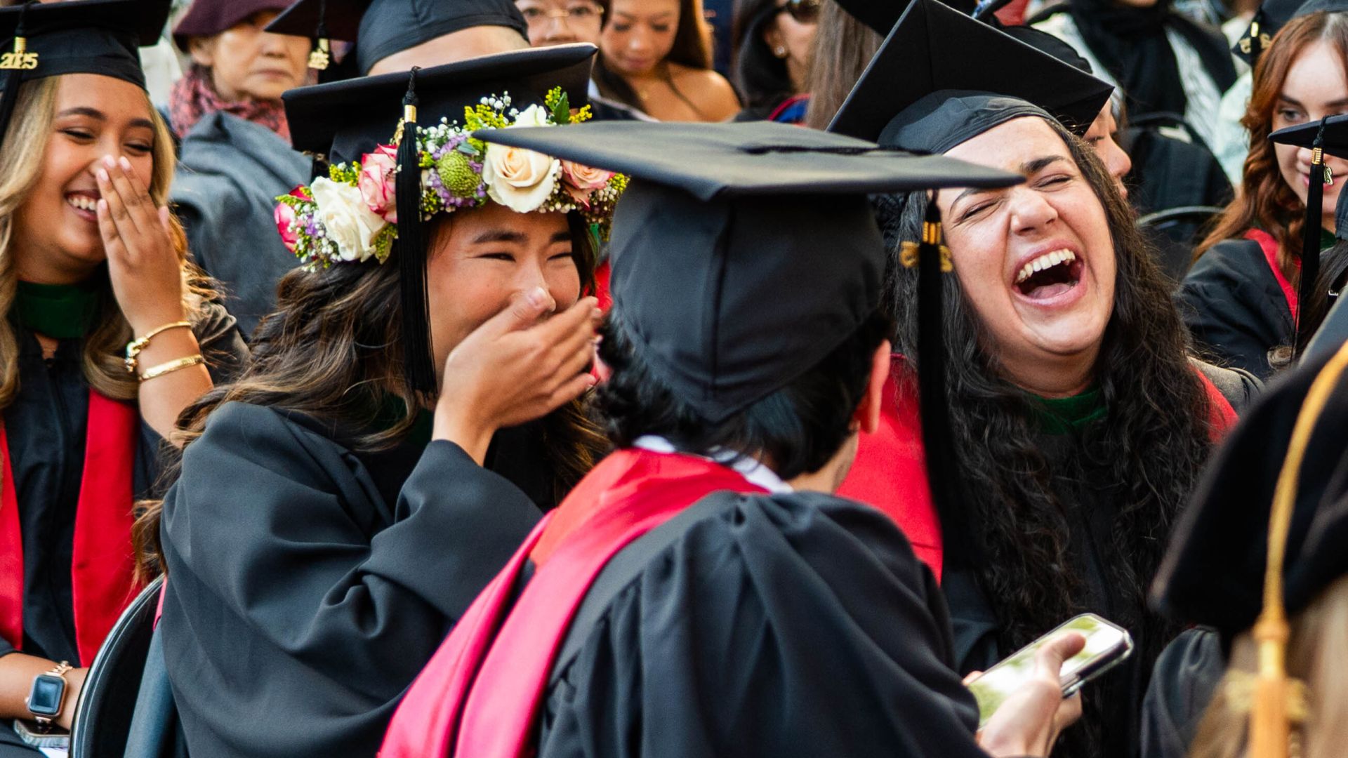 Members of the class of 2025, dressed in caps and gowns, laugh together at Commencement.