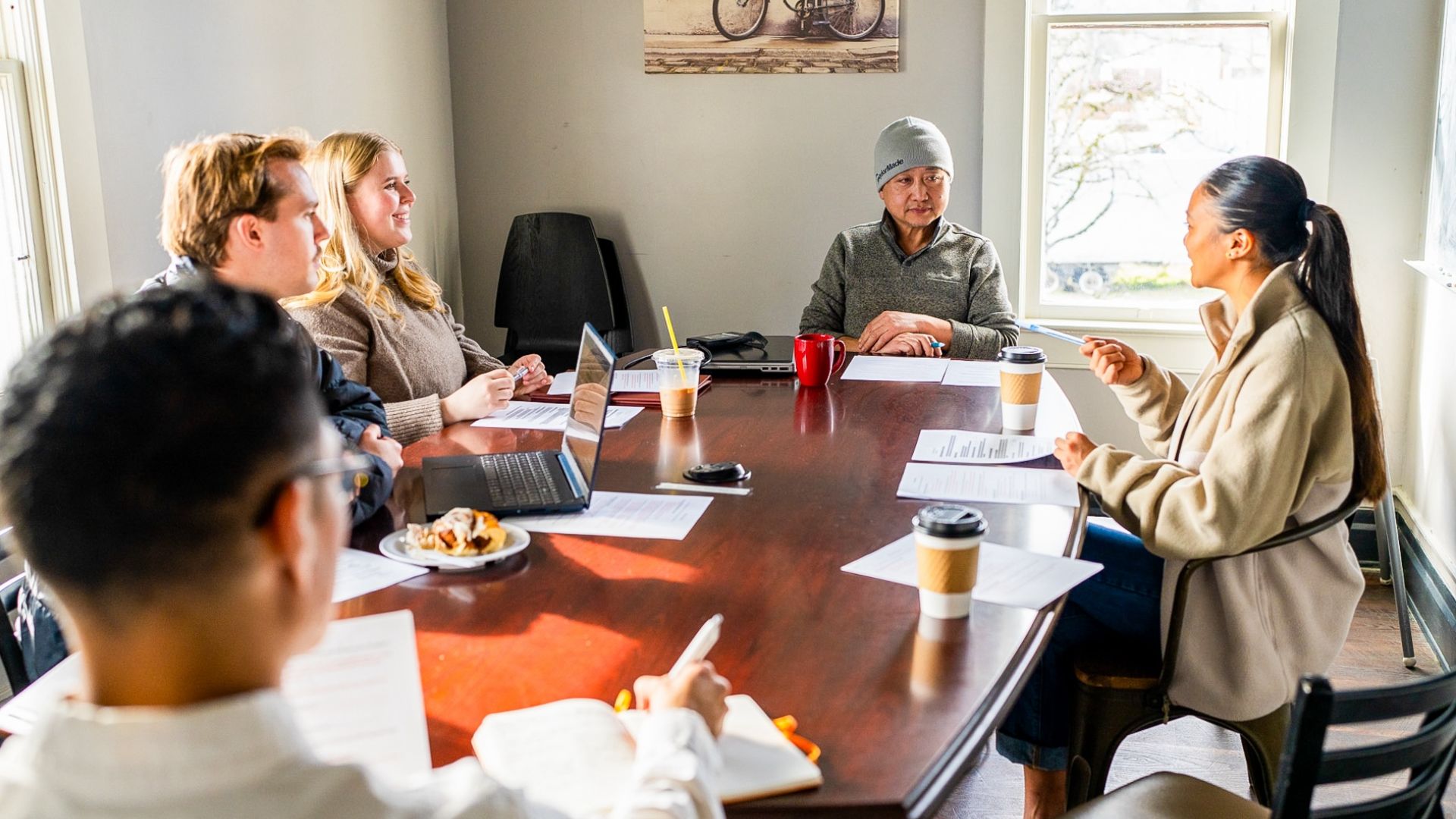 A group of Pacific students meet around a wooden table with representatives from a local business.