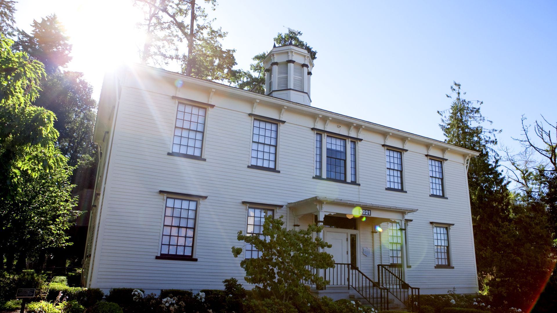 Photograph of Old College Hall in the summer with the sun shining just above the upper left corner of the building
