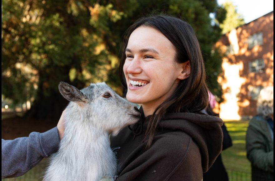 A student wearing a black hoodie smiles while holding a small goat