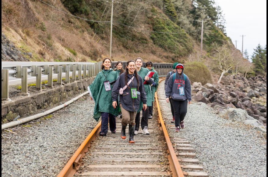 A group of Pacific biology students walks along railroad tracks near the beach